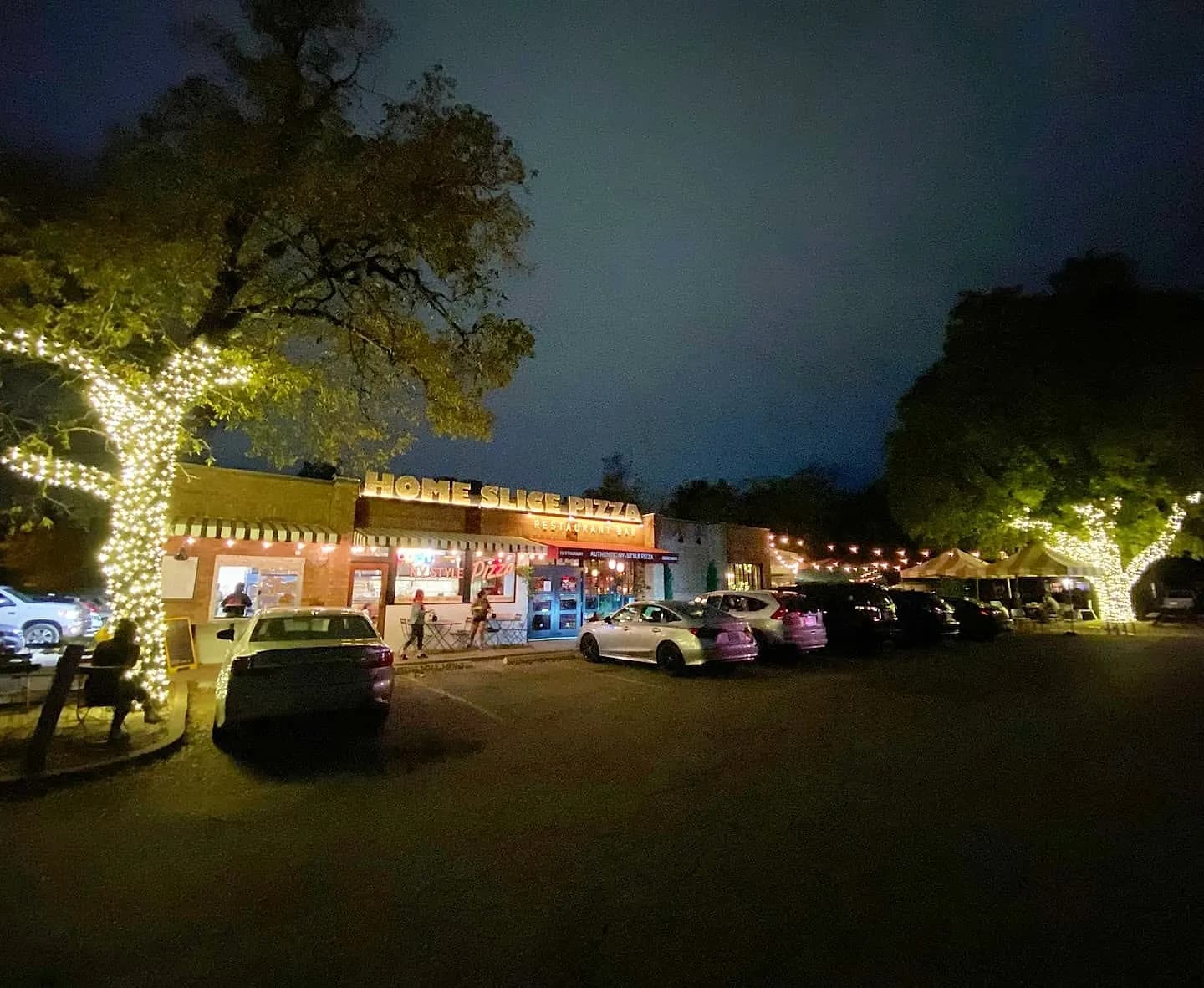Commercial strip with wrapped trees and roofline lights at night