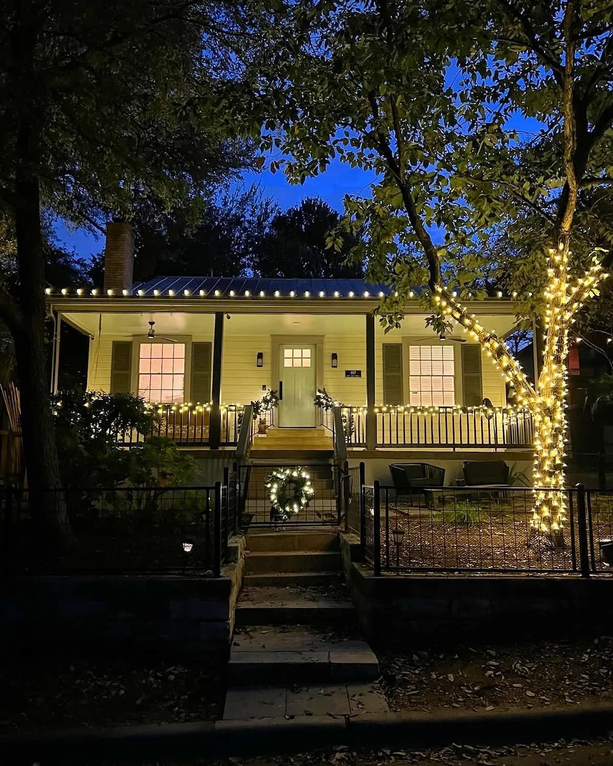 Front porch with lit garland, a door wreath and a wrapped tree beside the steps