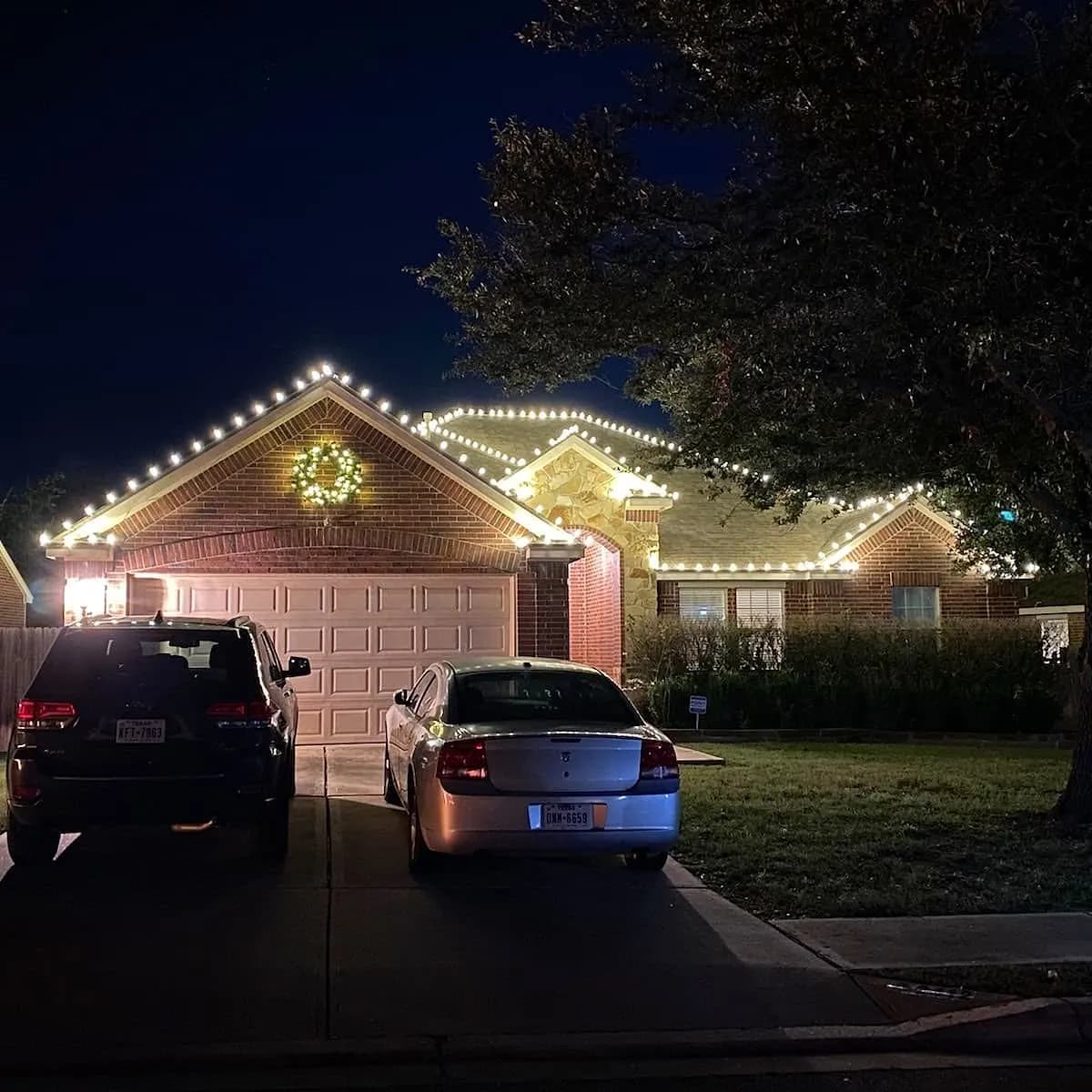 Warm white roofline lights with a lit wreath centered on the front gable