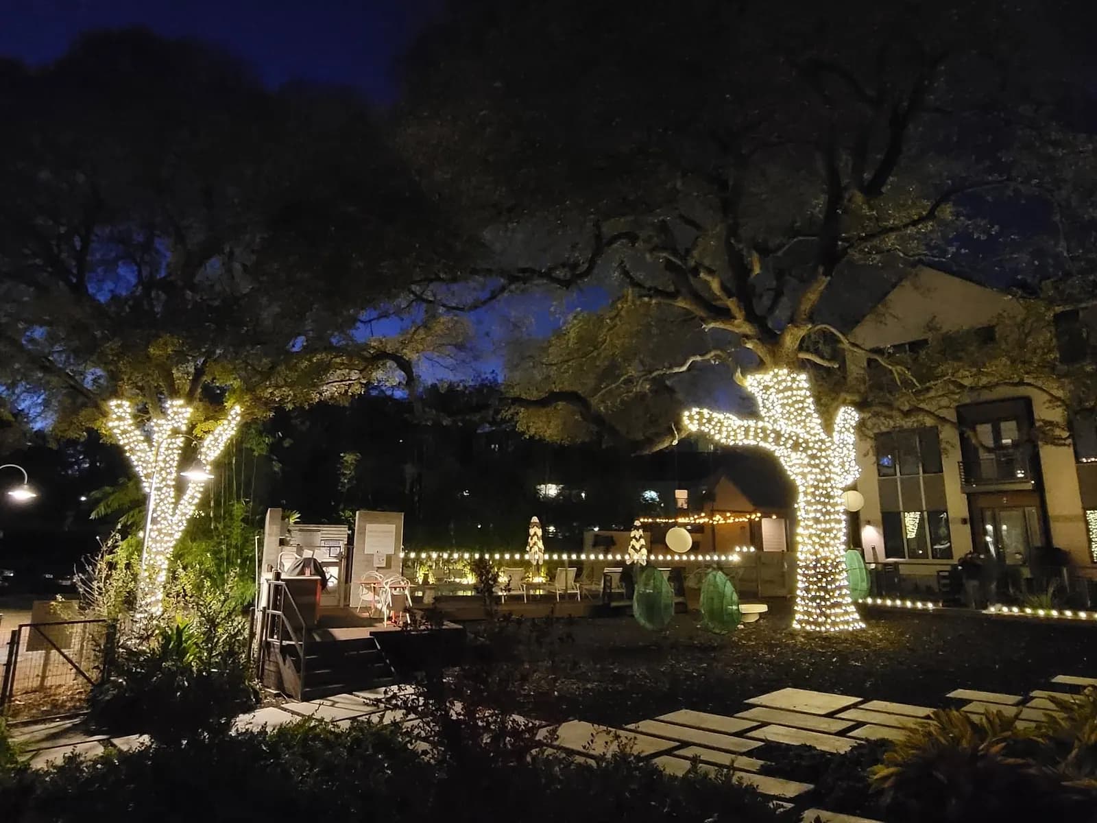 Live oaks wrapped in warm white lights over a stone courtyard